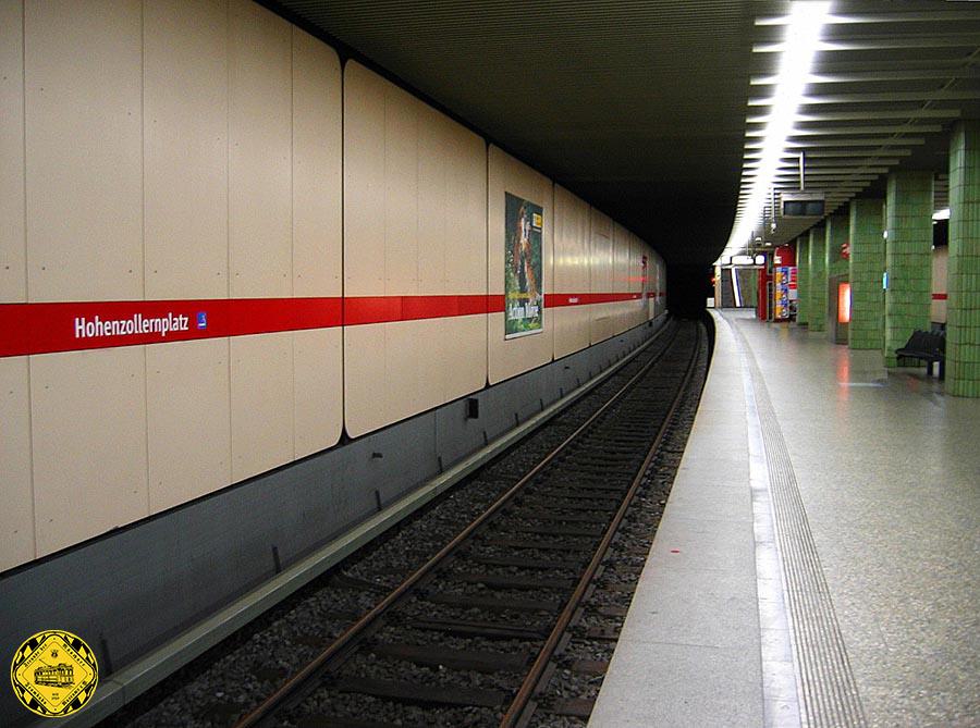 Der Bahnhof liegt in einer leichten Kurve in Nord-Süd-Richtung unter dem namensgebenden Hohenzollernplatz. Er wurde am 18. Oktober 1980 eröffnet und gleicht den anderen in den 1980er Jahren gebauten Bahnhöfen, da die Hintergleiswände mit graubeigen Wandpaneelen verkleidet sind. Der Boden besteht aus Isarkiesel-Kunststeinen, die Säulen wurden mit roten Paneelen gefliest und die Decke wurde mit Aluminium-Lamellen verblendet, über denen sich die Lichtbänder befinden. Vom südlichen Bahnsteigende gelangt man über ein Sperrengeschoss an die Oberfläche zur Kreuzung Teng- /Hohenzollernstraße, wo die Tramlinien 12 und 27, sowie die Metrobusse 53 und 59 verkehren. Am nördlichen Bahnsteigende gelangt man über das Sperrengeschoss zur Kreuzung Erich-Kästner-Straße/Herzogstraße.

© Bilder & Text: Florian Schütz | u-bahn-muenchen.de