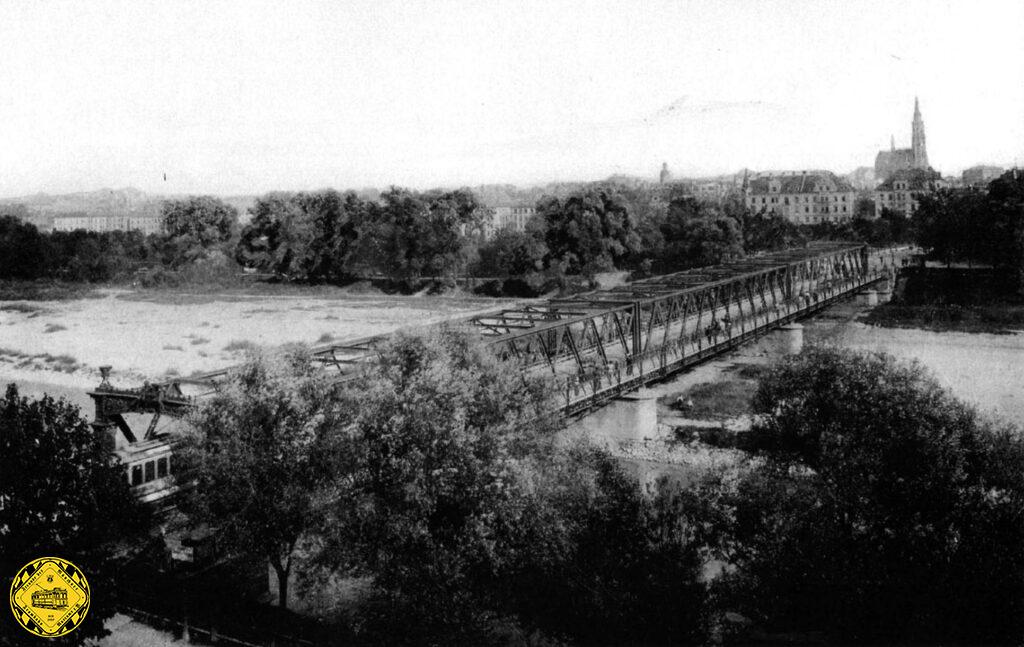 Links kann man gerade noch einen Wagen der weißen Linie erkennen, der über die alte Wittelsbacher Brücke gefahren ist und auf den Baldeplatz kommt. Im Hintergrund die gerade fertig gewordenen Giesinger Kirche.