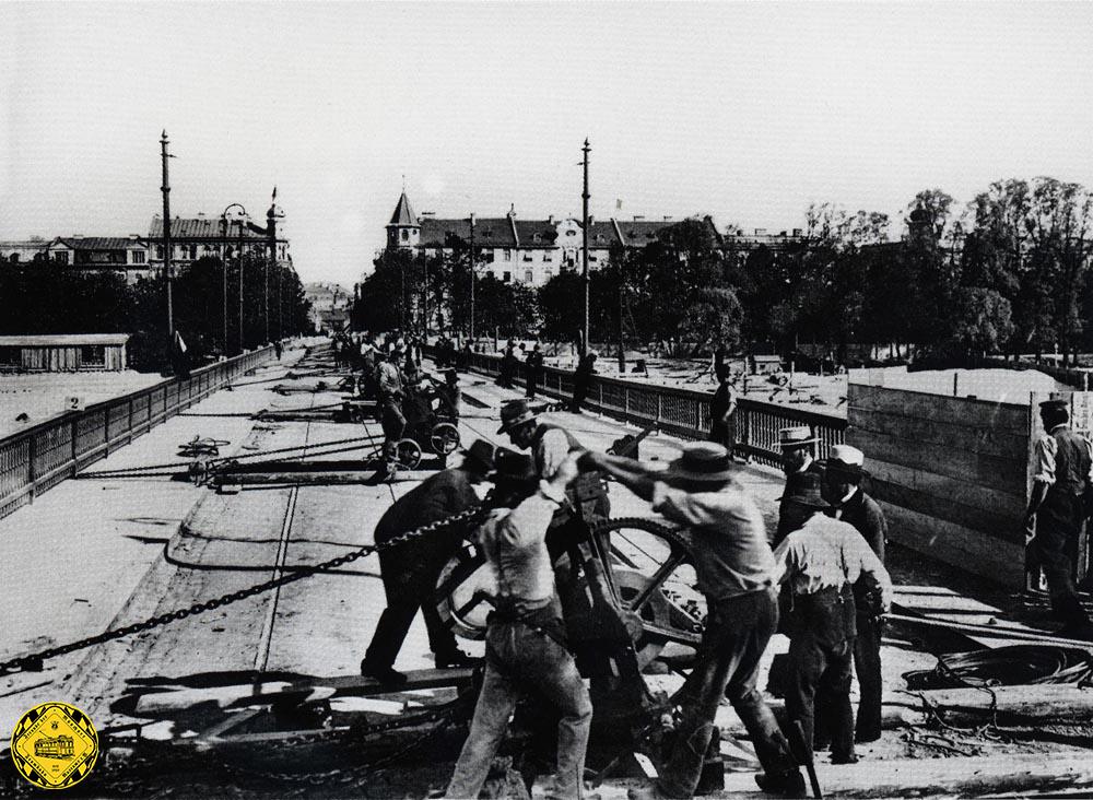 Um 5 Uhr nachmittags am Dienstag, den 3.Juni 1902, begannen 250 Arbeiter die Reichenbachbrücke auf vorbereiteten Holzunterbau auf 14cm dicken Eisenkugeln mit Winden Richtung Süden Isar-aufwärts zu ziehen. Gut sieht man hier die Trambahnschienen in der Brückenmitte.
