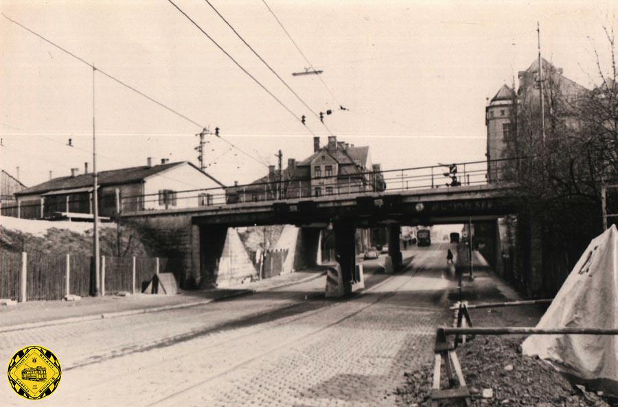 Unser Bild ist datiert mit 1955 und zeigt daher sogar noch die Doppeloberleitung des O-Bus, der zur Wolfratshauserstraße fuhr. Hier kann man auch gut sehen, dass es sich eigentlich um 2 Brücken handelt, die der Hauptbahnstrecke und die des aufgelassenen Industriegleises in das Sendlinger Oberfeld.