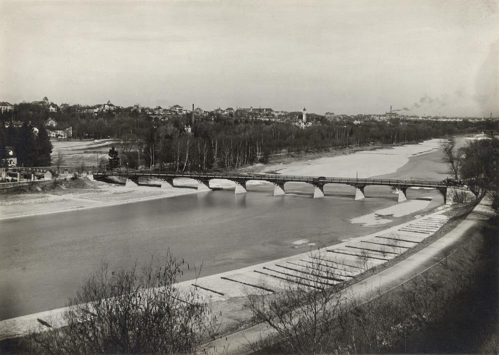 Unser Bild zeigt eine Ansichtskarte mit der Thalkirchnerbrücke (Tierparkbrücke) aus dem Jahr 1910. Zu diesem Zeitpunkt wurde der Tiergarten, später der Tierpark Hellabrunn, eröffnet. 