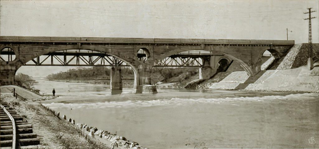 Auf dem Bild kann man noch links die Schienen der Bau-Bahn zu dieser Baustelle sehen und die Leinthaler Straßenbrücke hinter der Eisenbahnbrücke Isar-aufwärts, die hier schon sein 1903 stand.