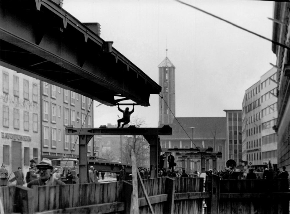 1966 11 19 Aufbau Stahlhochbrücke Von Der Tann Str Ludwigstr (11) Die ersten Brückenelemente für den Mittelteil sind 30m lang und 55 Tonnen schwer. Danach werden mit einem zweiten Autokran die weiteren Brückenelemente in beide Richtungen bis zu den Rampen eingesetzt. Am Abend des 19.November 1966 sind dies Arbeiten komplett abgeschlossen. 