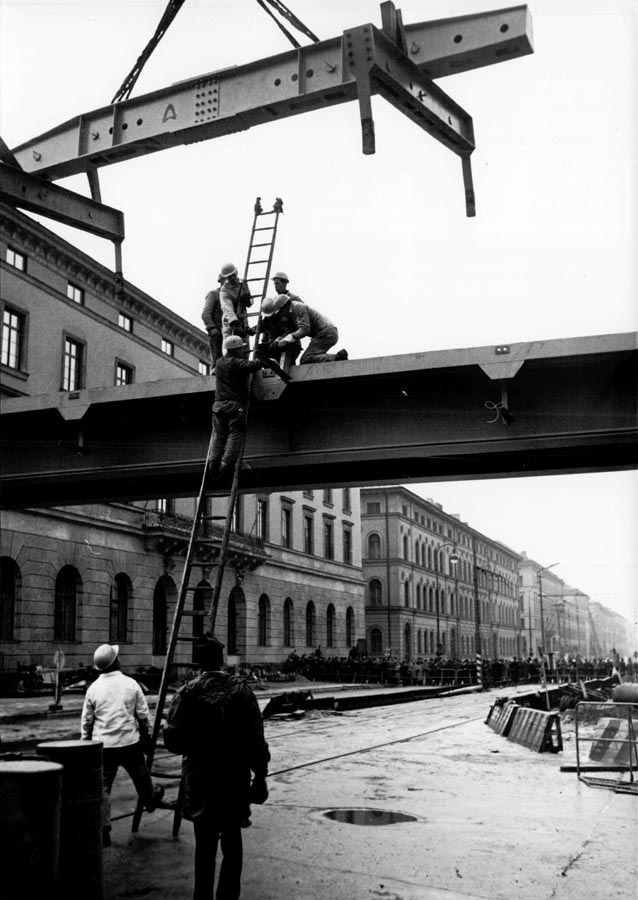 1966 11 19 Aufbau Stahlhochbrücke Von Der Tann Str Ludwigstr (17) Die ersten Brückenelemente für den Mittelteil sind 30m lang und 55 Tonnen schwer. Danach werden mit einem zweiten Autokran die weiteren Brückenelemente in beide Richtungen bis zu den Rampen eingesetzt. Am Abend des 19.November 1966 sind dies Arbeiten komplett abgeschlossen. 