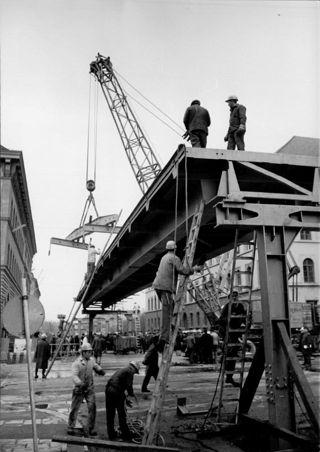 1966 11 19 Aufbau Stahlhochbrücke Von Der Tann Str Ludwigstr (19) Die ersten Brückenelemente für den Mittelteil sind 30m lang und 55 Tonnen schwer. Danach werden mit einem zweiten Autokran die weiteren Brückenelemente in beide Richtungen bis zu den Rampen eingesetzt. Am Abend des 19.November 1966 sind dies Arbeiten komplett abgeschlossen. 