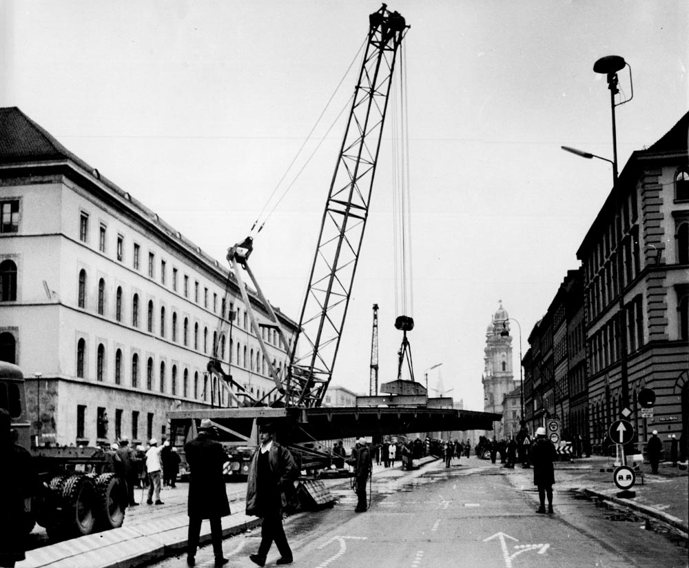 1966 11 19 Aufbau Stahlhochbrücke Von Der Tann Str Ludwigstr (23) Die ersten Brückenelemente für den Mittelteil sind 30m lang und 55 Tonnen schwer. Danach werden mit einem zweiten Autokran die weiteren Brückenelemente in beide Richtungen bis zu den Rampen eingesetzt. Am Abend des 19.November 1966 sind dies Arbeiten komplett abgeschlossen. 