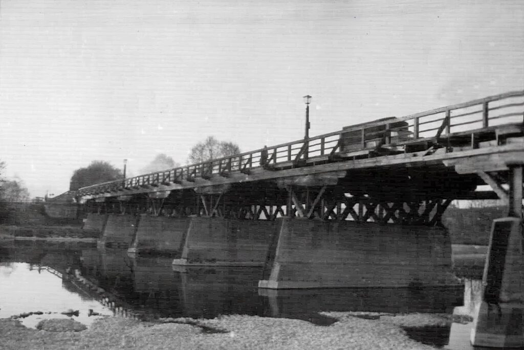 Eine Brücke mit einer interessanten Vergangenheit. Den 2.Weltkrieg hat die Holzkonstruktion überlebt. Anfang September 1944 riss eine Bombe ein etwa ein Meter großes Loch in die Brücke.  Wie man auf dem Bild von 1949 sehen kann, war ein Betrieb aber weiterhin möglich. 